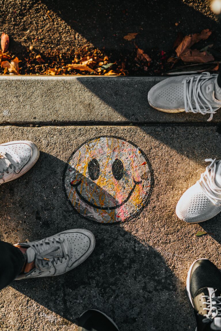 A group of individuals' feet around a smiley face drawn on the ground
