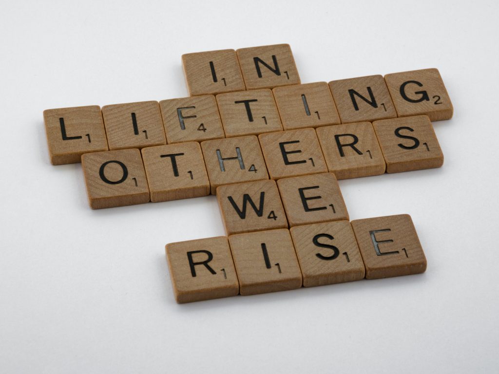 In scrabble tiles the words: "In Lifting others we rise" are written