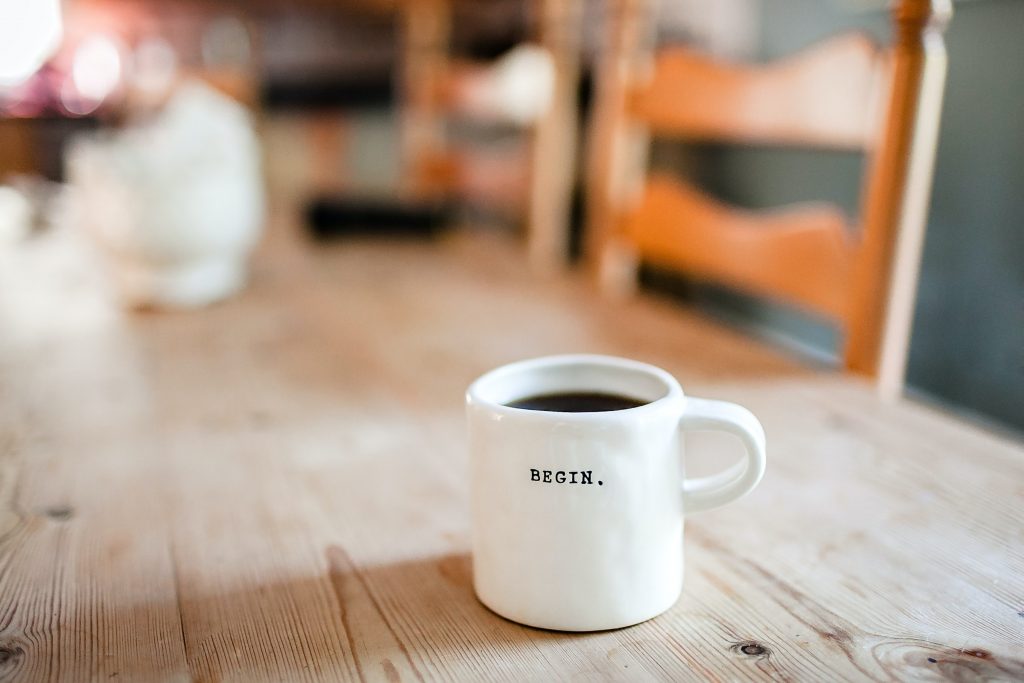 Coffee mug on the table in focus with the word "begin" written on it