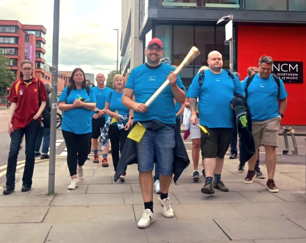 A man in a blue shirt and blue shorts holding a baton for Baton of Hope 2023