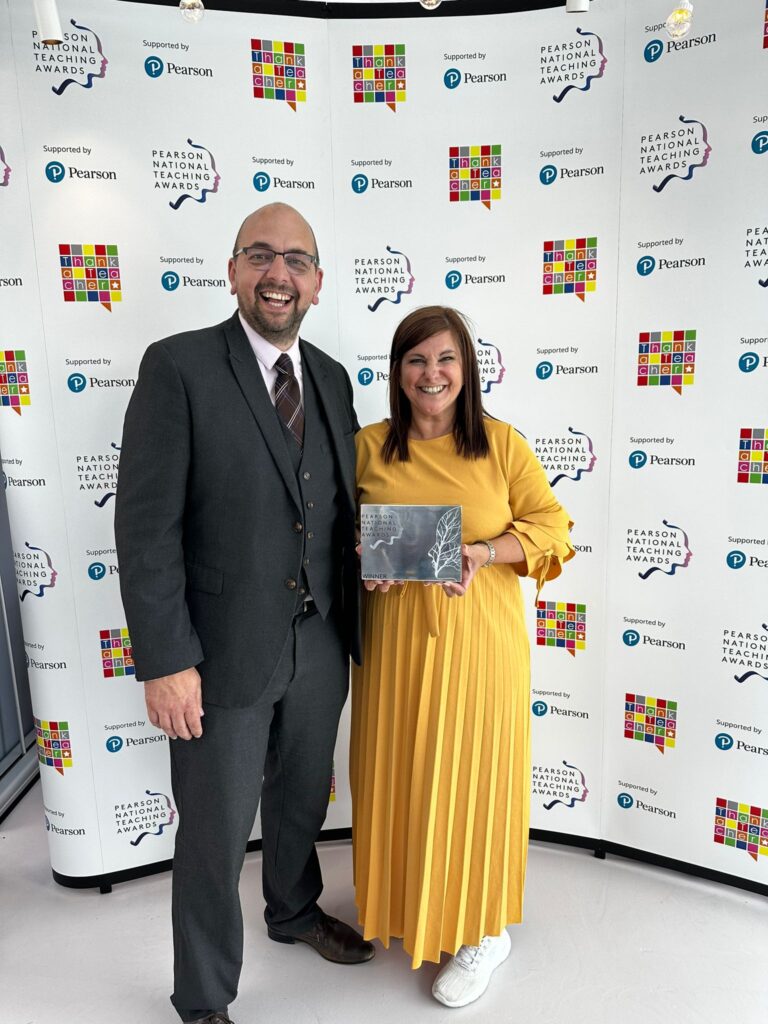 2 individuals smiling towards a camera holding the pearsons silver award