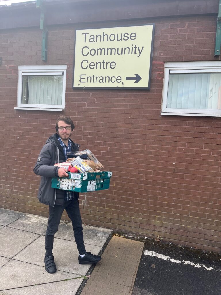 A man walking outside of the Tanhouse Community Centre holding a basket of groceries