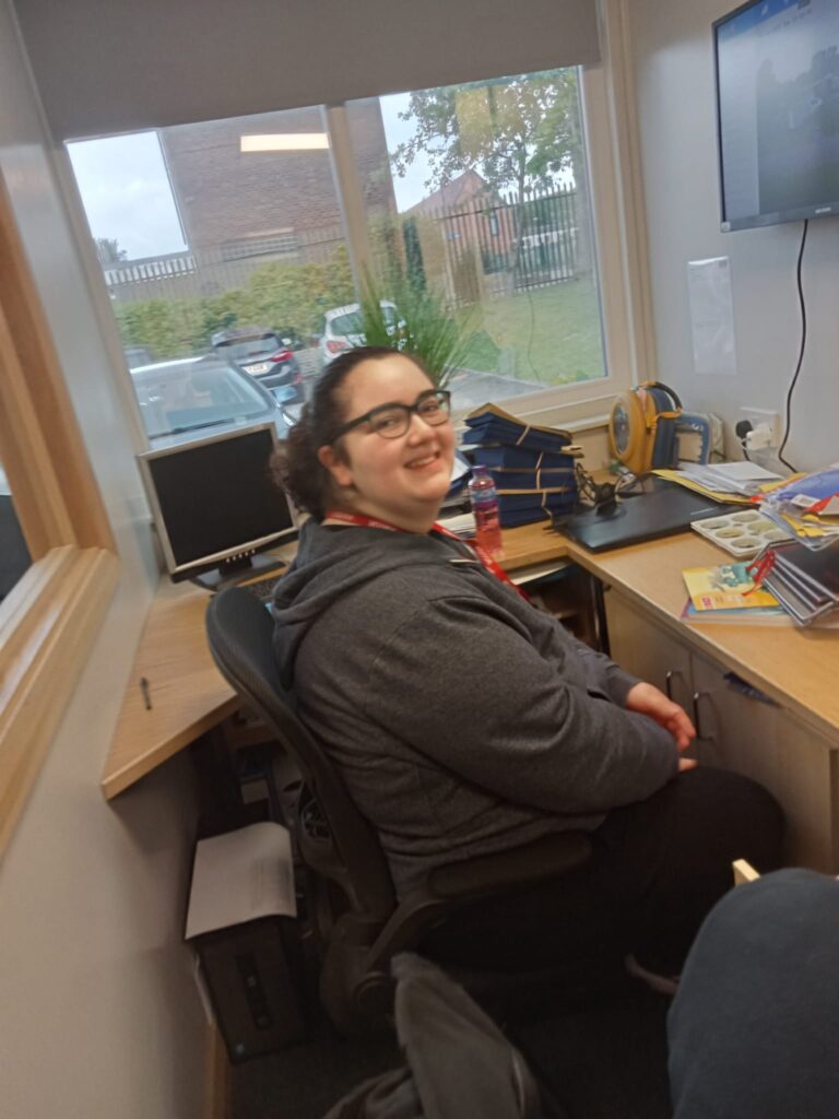 An individual smiles at a desk inside a primary school