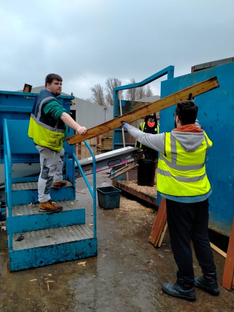 2 workers holding a piece of lumber as a third watches in the background